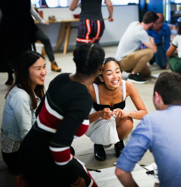 Woman in a black top and skirt crouching down talking to two other people in a circle.